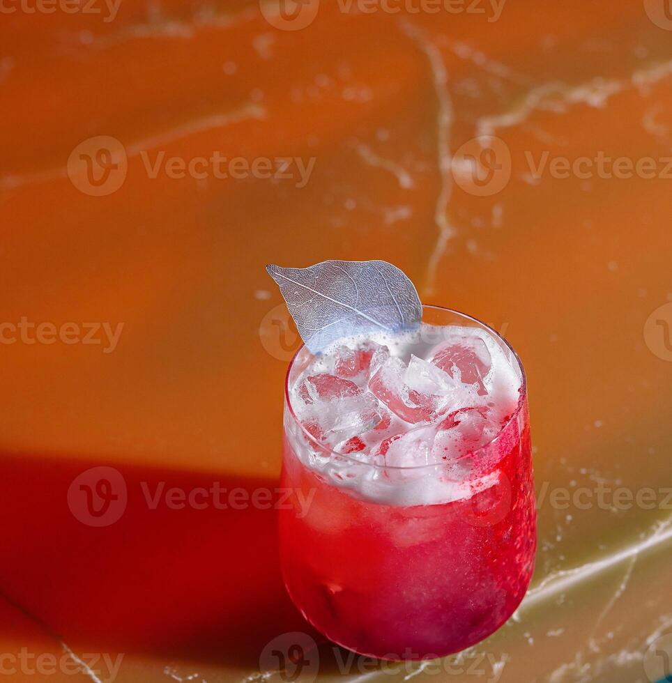 Red cocktail standing on bar countertop with silver leaf garnish photo