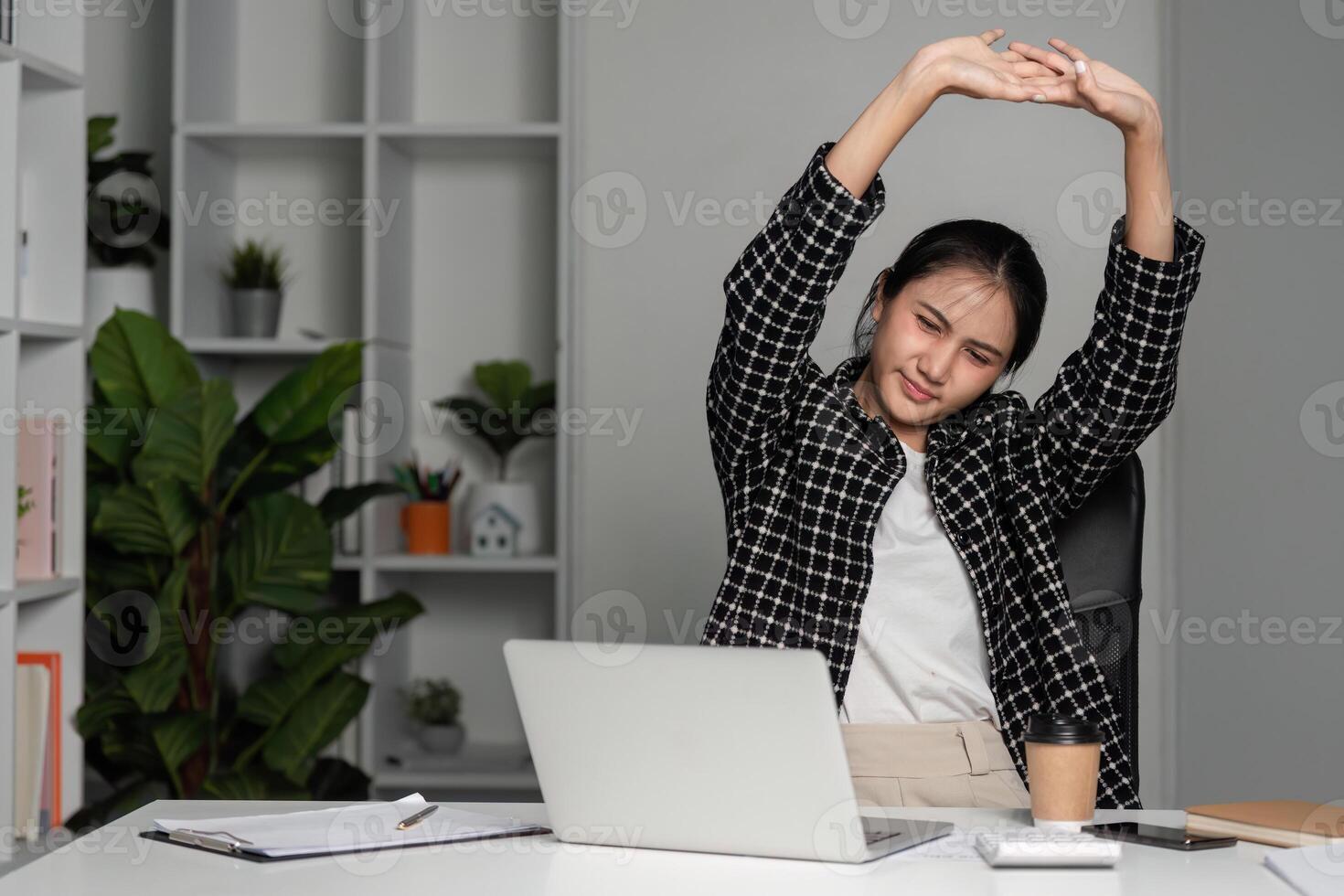 Young Female Accountant Stretching at Desk, Tired from Work in Modern Office Setting with Laptop and Documents photo