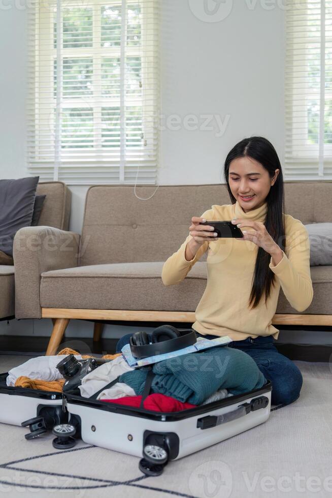 Young Woman Packing Clothes into a Suitcase While Sitting on the Floor in a Modern Living Room photo