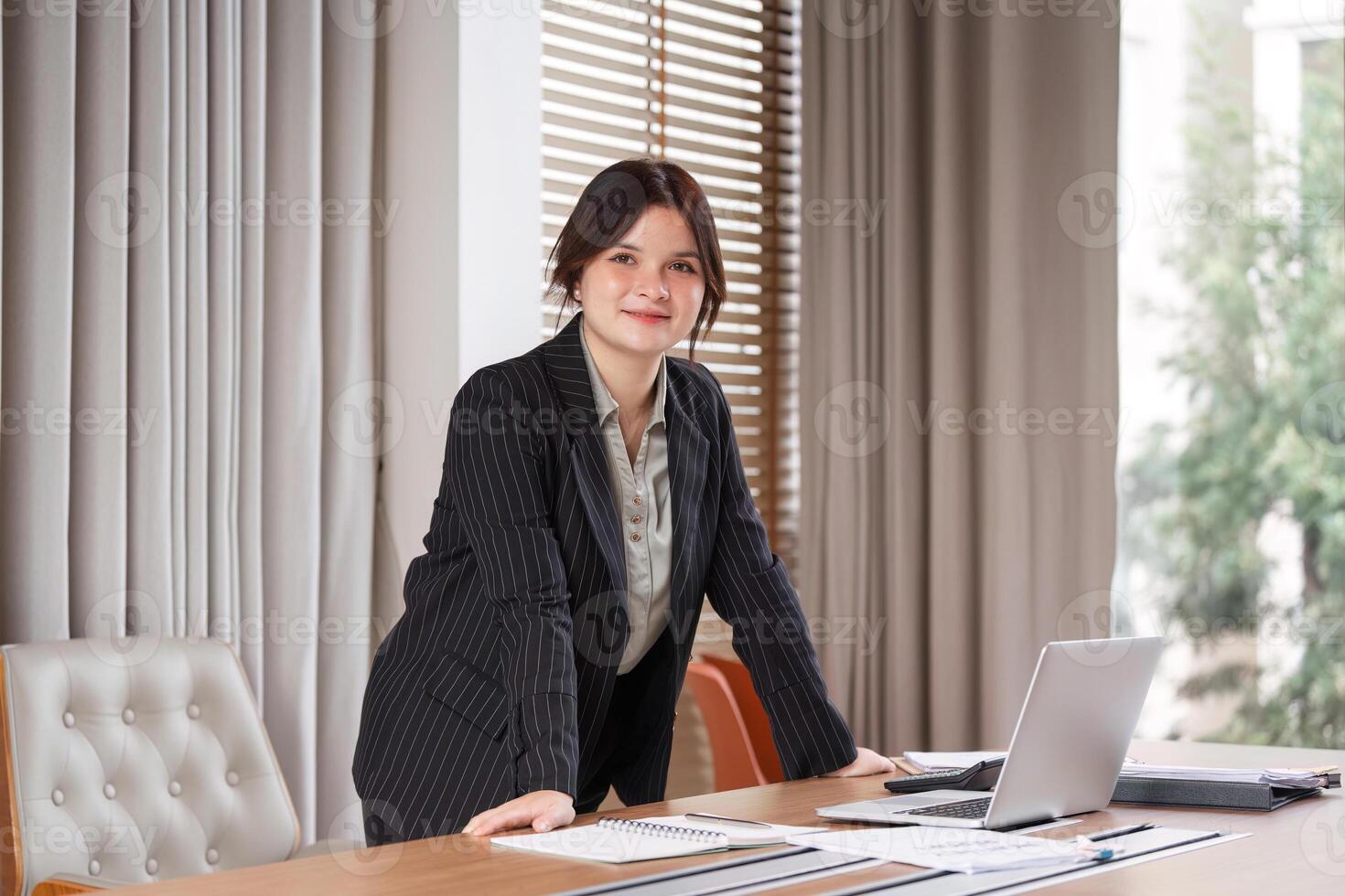 Confident Businesswoman in Modern Office Setting with Laptop and Documents on Desk, Professional Attire, Bright and Motivated Atmosphere photo