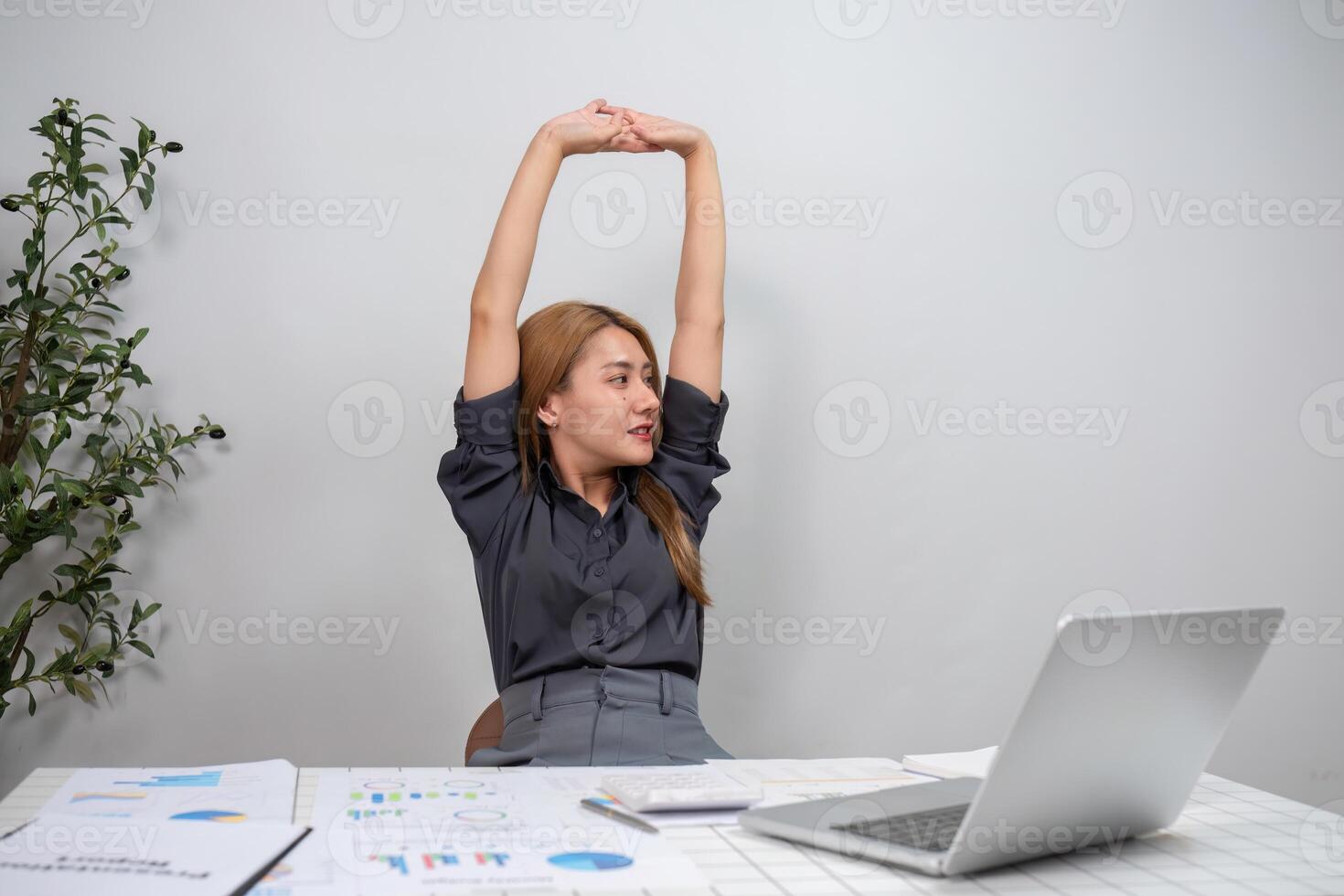 Young Female Employee Stretching at Desk, Tired from Work, Office Environment, Business Charts and Laptop, Modern Workplace photo