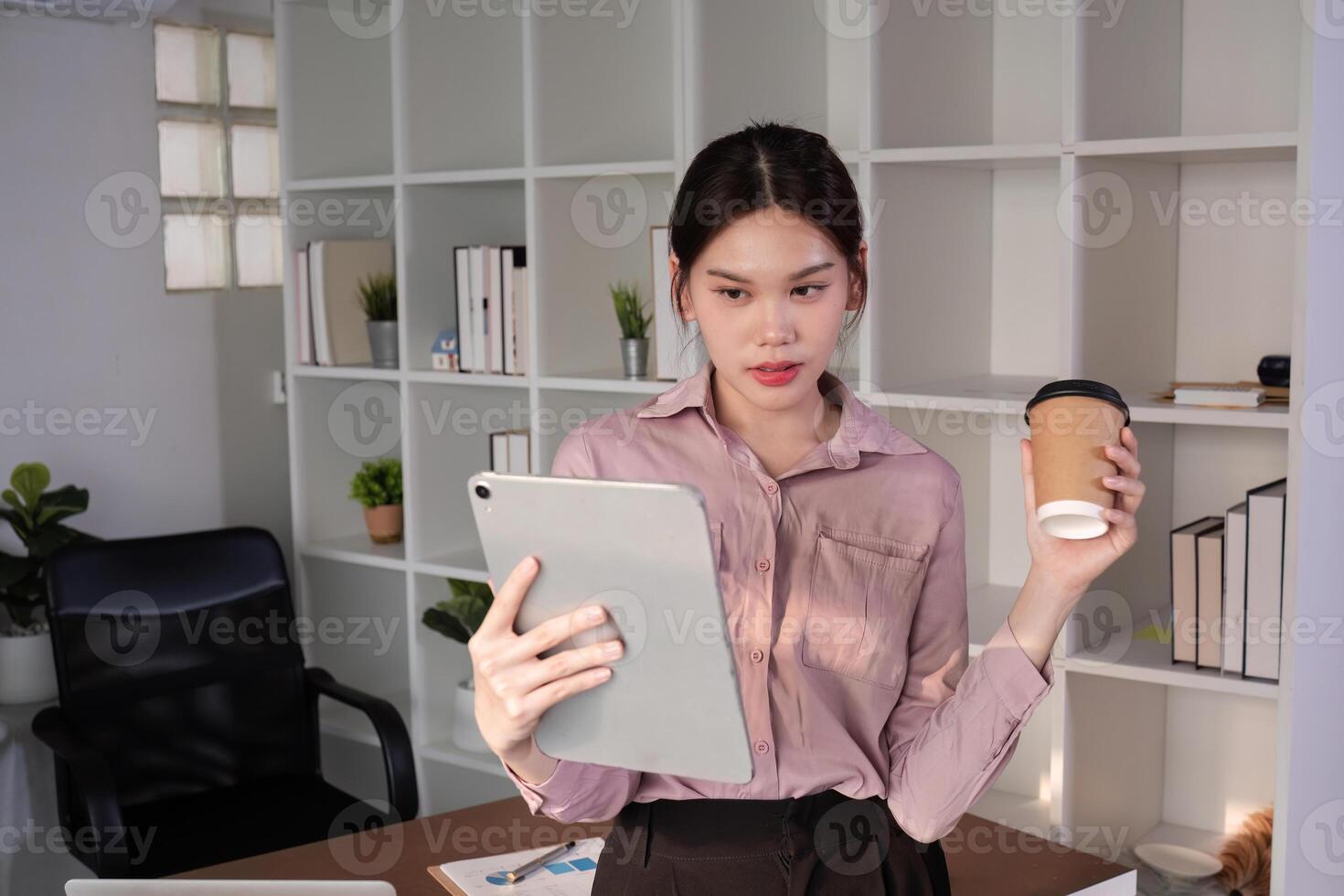 Young Accountant Using Tablet to Communicate with Clients in Modern Office Setting, Holding Coffee Cup photo