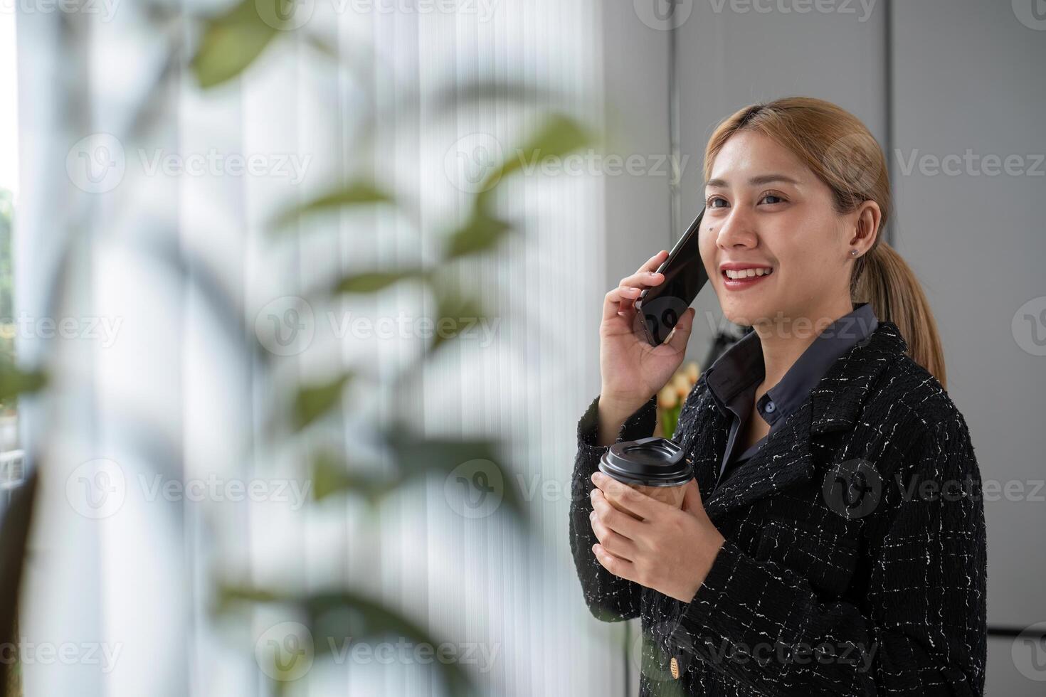Confident Business Woman Talking on Phone While Holding Coffee in Modern Office Setting photo