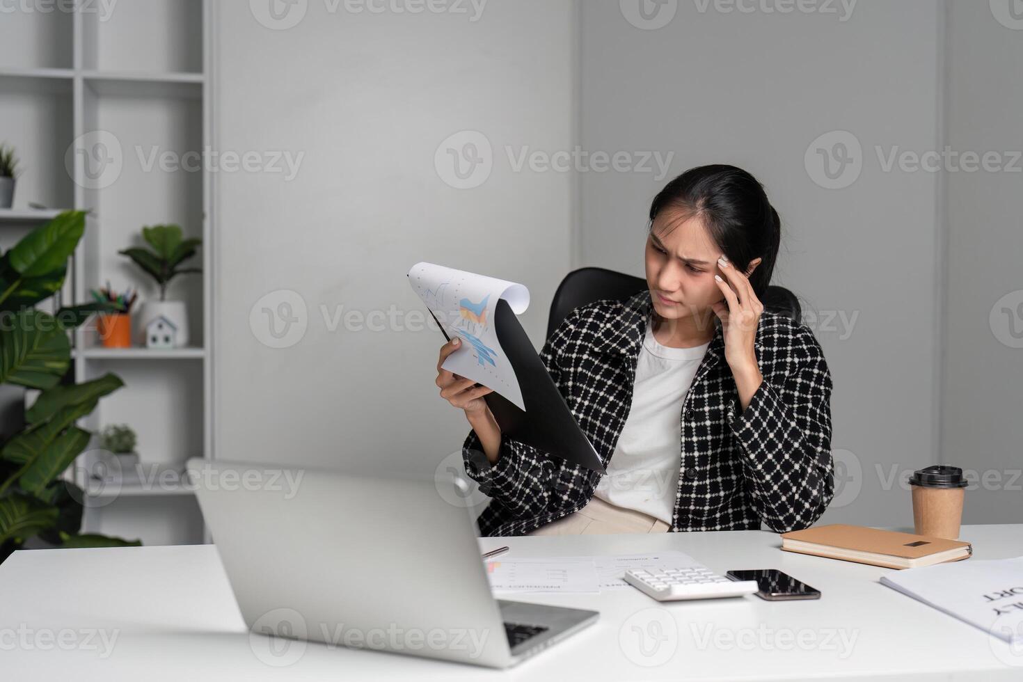Stressed Office Worker Reviewing Documents at Desk with Laptop and Coffee in Modern Workspace photo