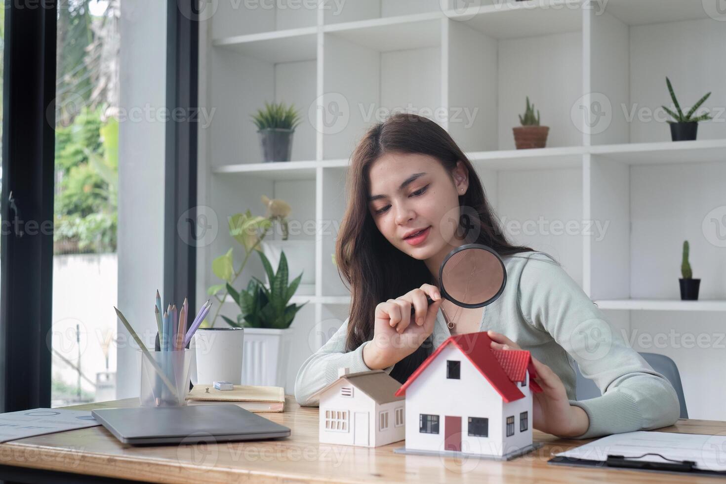 Real Estate Agent Analyzing Model Houses with Magnifying Glass in Modern Office Setting photo