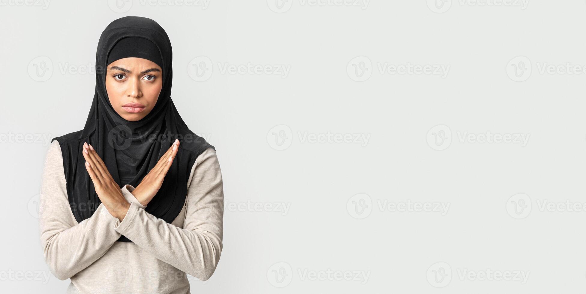 No racism. Angry afro muslim girl in hijab making denial hand gesture, keeping arms crossed over chest, rejecting something bad over gray background photo
