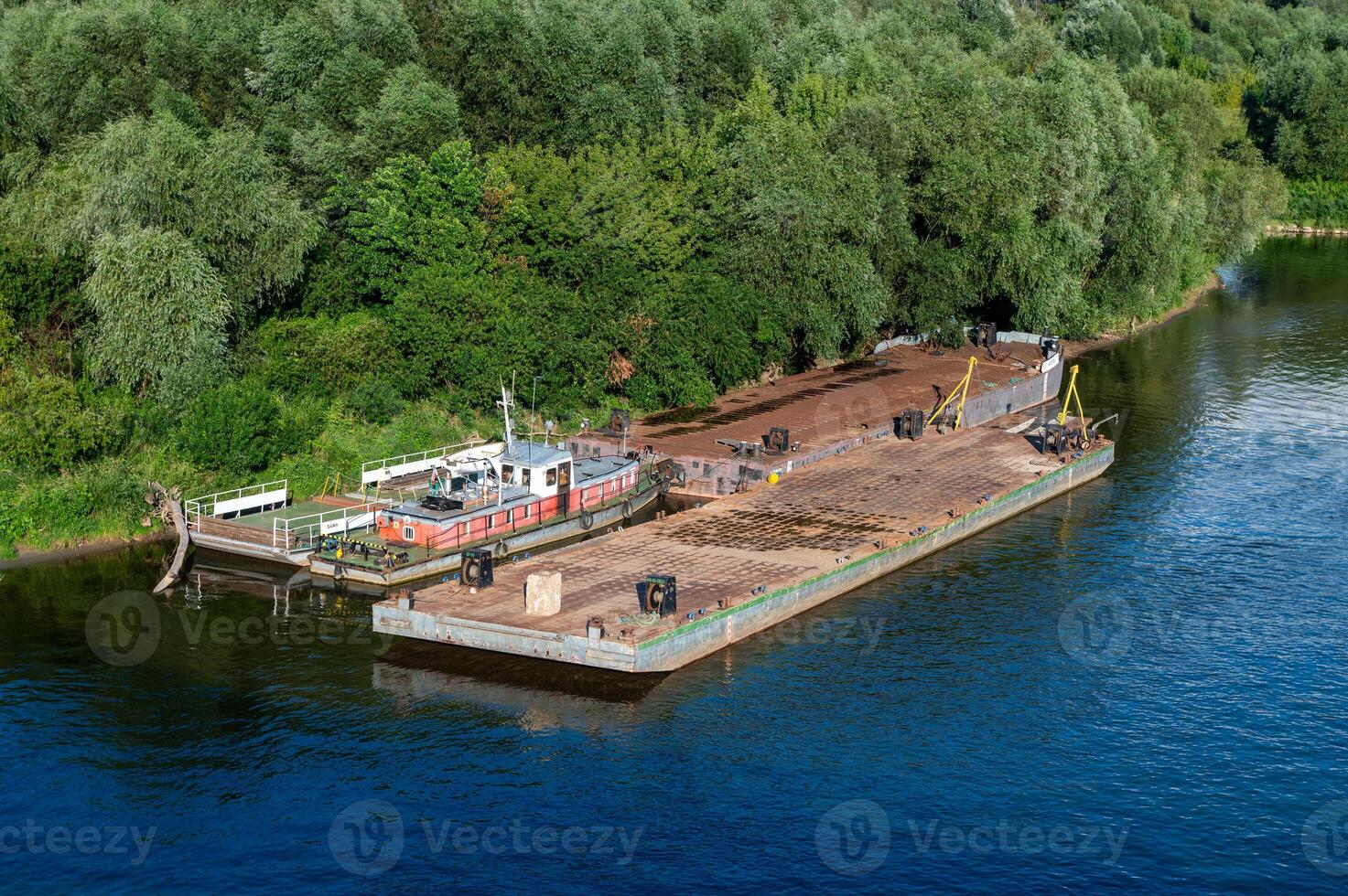 Docked barge and small boat by a green forested riverside. photo