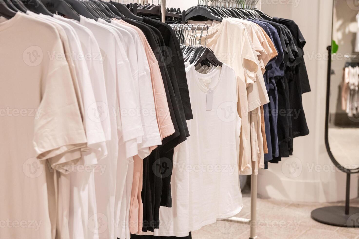 Various t-shirts in neutral colors on hangers in retail clothing store. photo