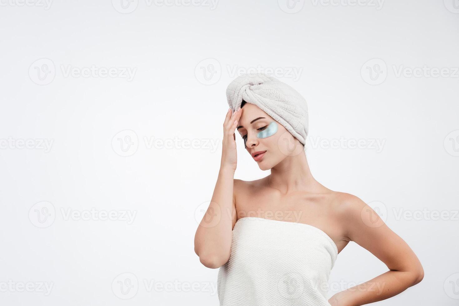 A beautiful woman with blue eyes against a white background, wearing under-eye patches and a towel on her head. Cosmetology ads concept. Healthy, glow skin. Free copy space, banner photo
