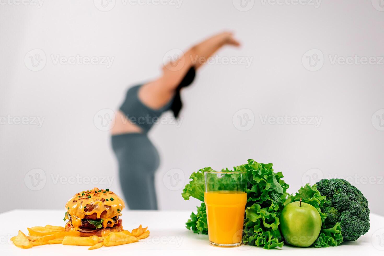 Beautiful, full-figured woman exercising on a light background with a burger and greens nearby. Perfect for promoting a healthy lifestyle and the balance between fitness and nutrition photo