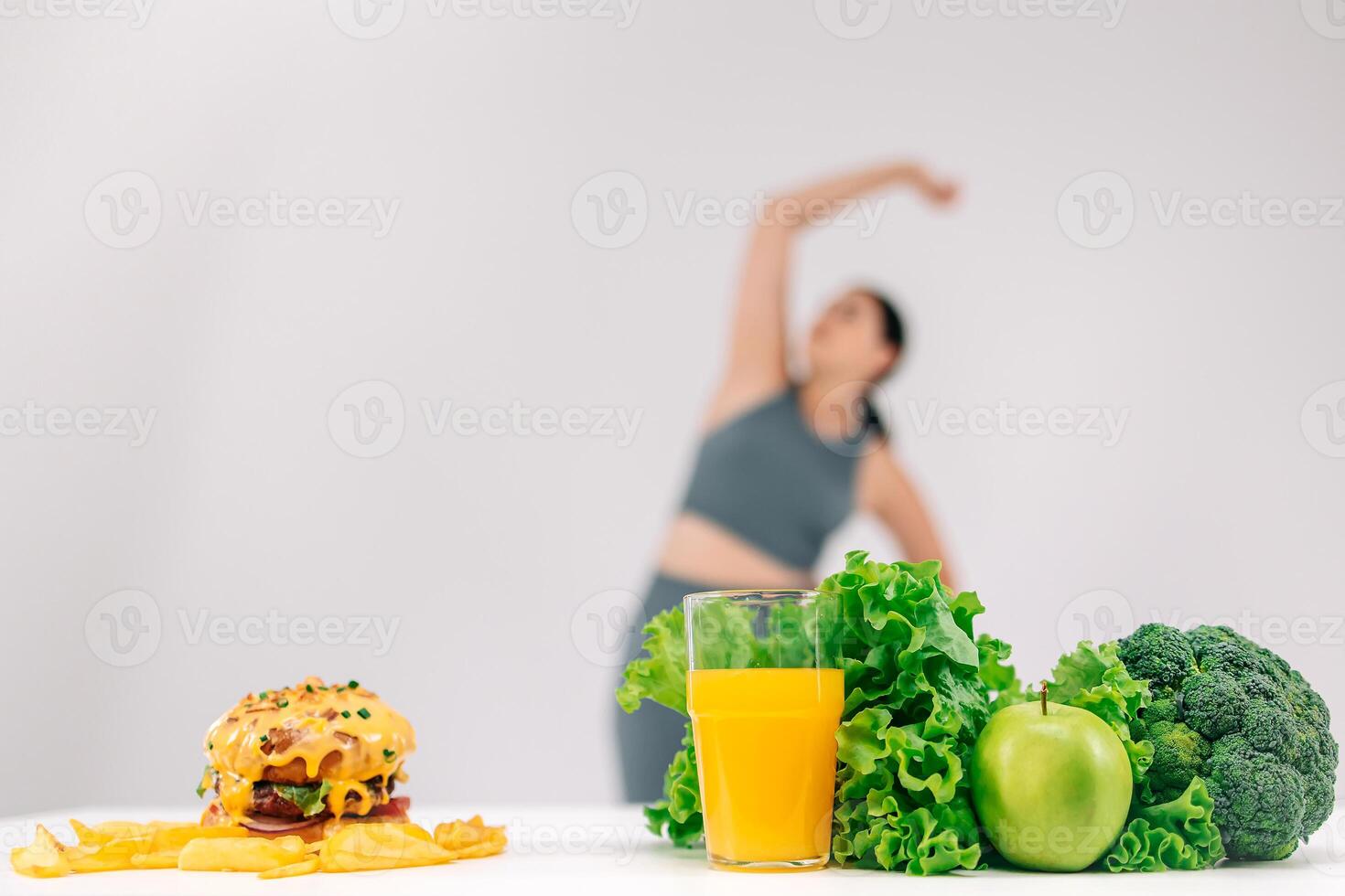 Full-figured woman on a light background talking on the phone with her dietitian, with a burger and healthy food nearby. Perfect for promoting conscious choices towards a healthier diet photo
