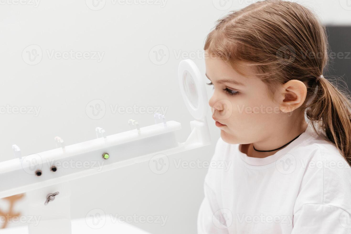 A little girl enjoys an engaging vision game on state-of-the-art ophthalmic equipment. The Rainbow system enhances eyesight in a comfortable and welcoming environment. photo