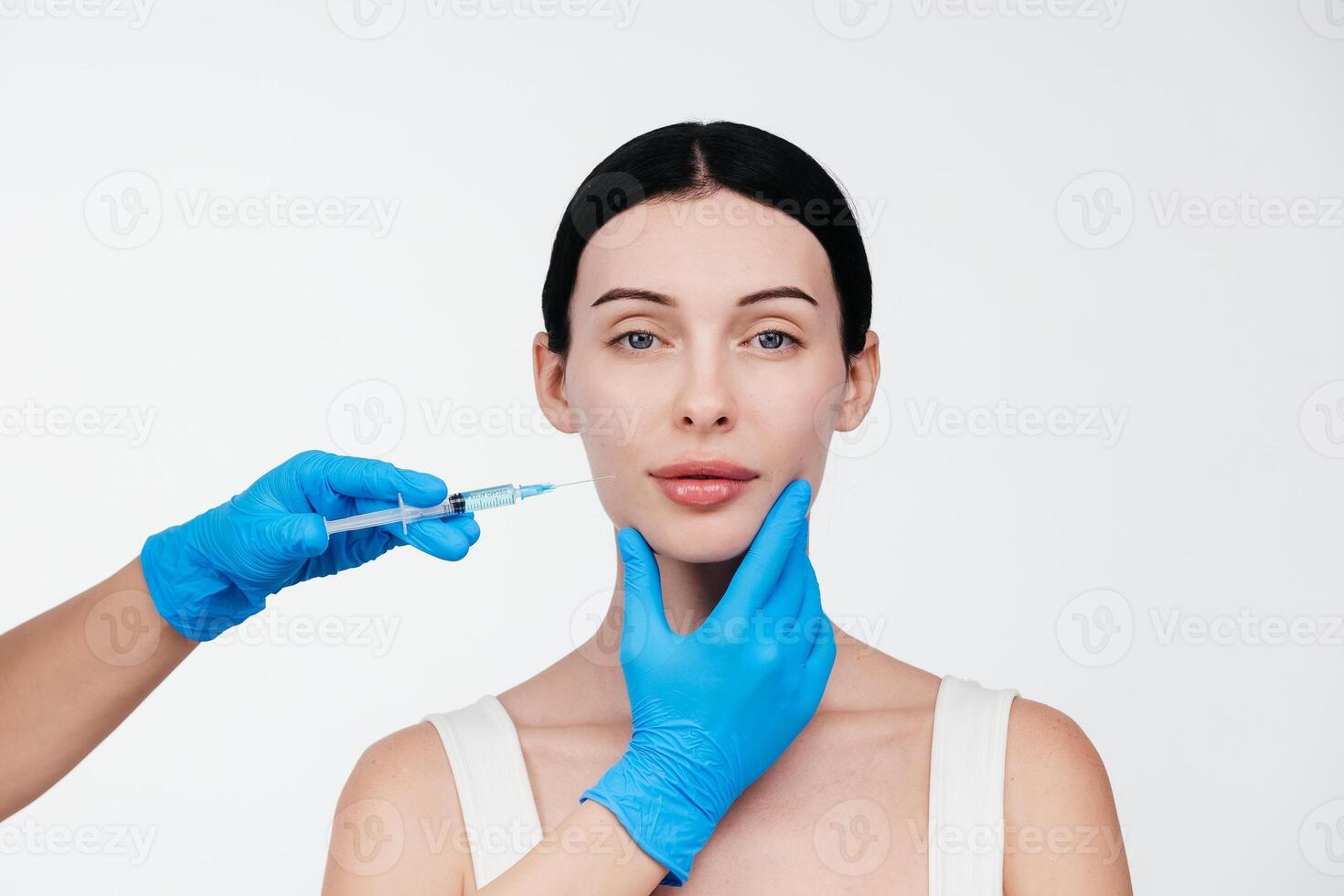 Unrecognizable lady receiving hyaluronic acid injection. Cropped picture of young woman standing isolated over white background. Doctor injecting in a beautiful face of a young woman. Plastic surgery photo