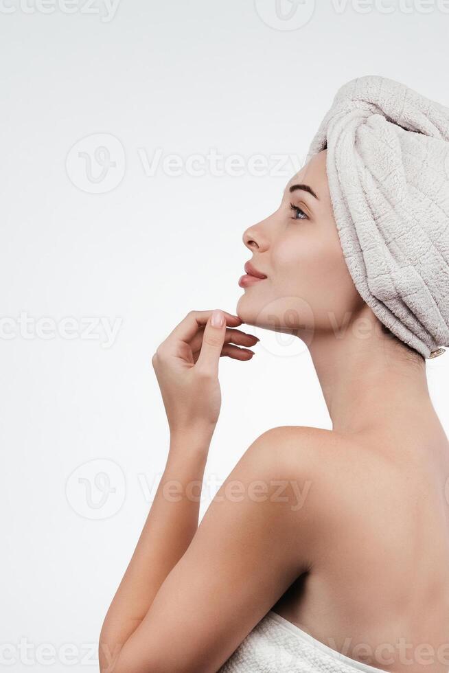 A woman with flawless skin wearing a hair towel after a spa treatment. Her relaxed expression evokes a sense of harmony and self-care against a white background photo