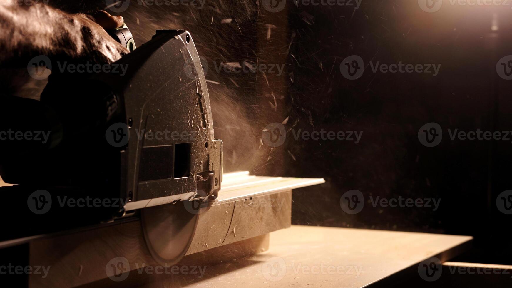 Close-up of a man cuts a wooden plank with an electric circular saw in a workshop. Cutting a piece of wood on a circular saw in backlight. Ideal topics related carpentry, efficient sawing techniques photo