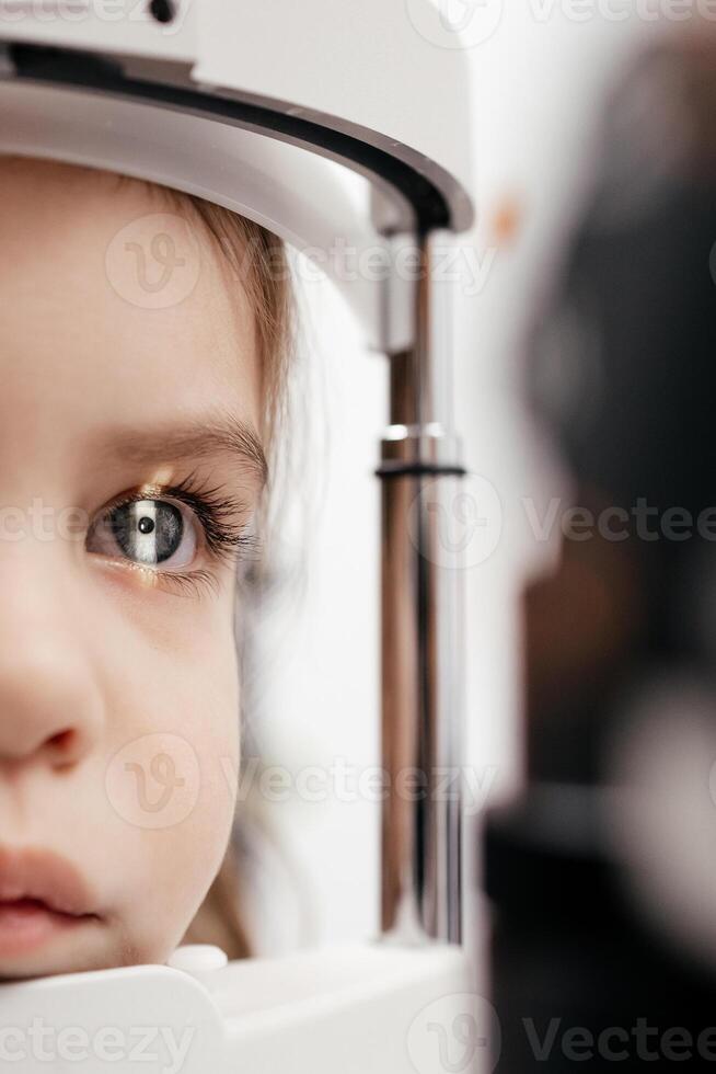 A little girl undergoes an eye test by a professional optometrist using modern diagnostic equipment in ophthalmology clinic. Beautiful female eye with yellow laser ray. Vision correction. Macro shot photo