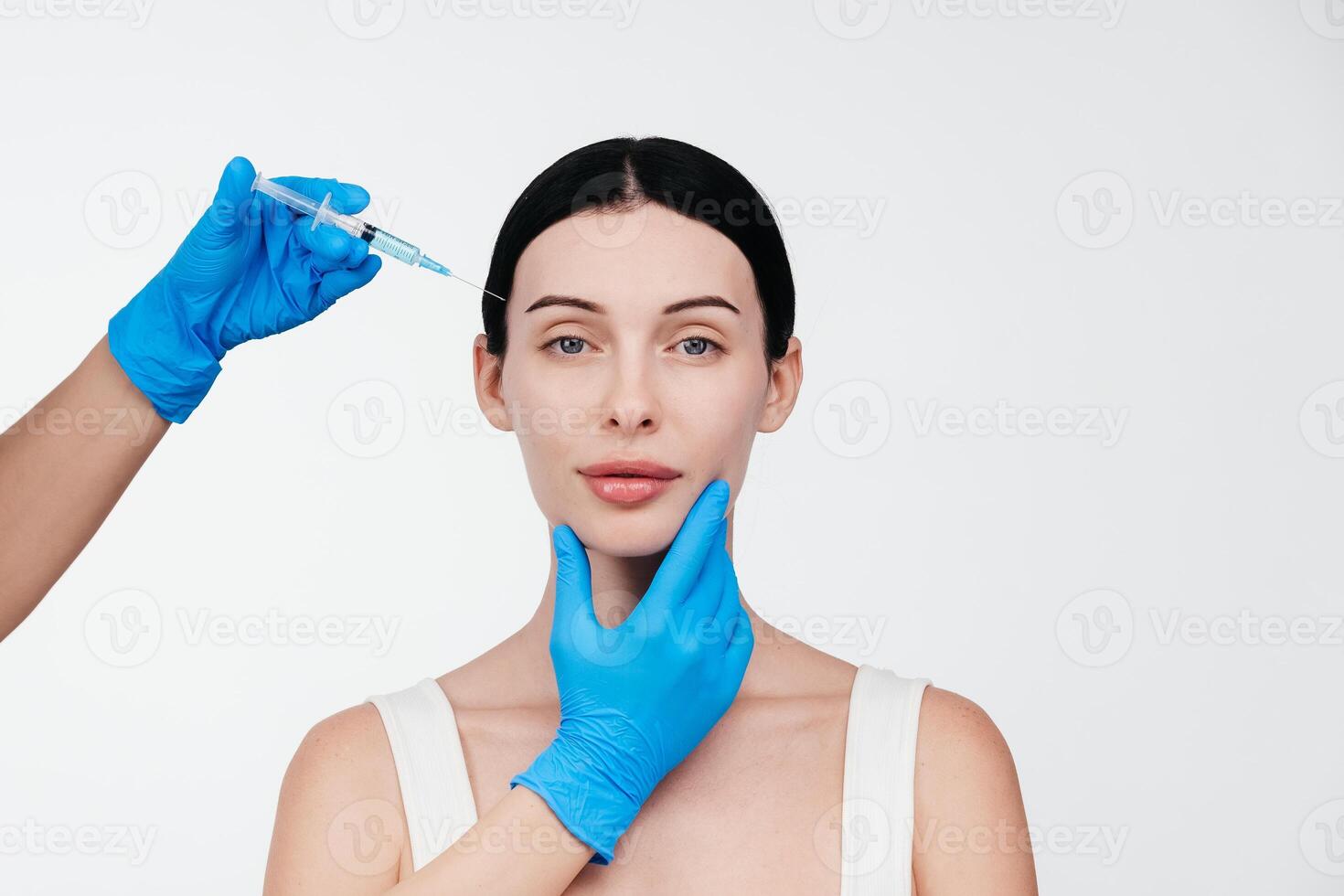 Unrecognizable lady receiving hyaluronic acid injection. Cropped picture of young woman standing isolated over white background. Doctor injecting in a beautiful face of a young woman. Plastic surgery photo