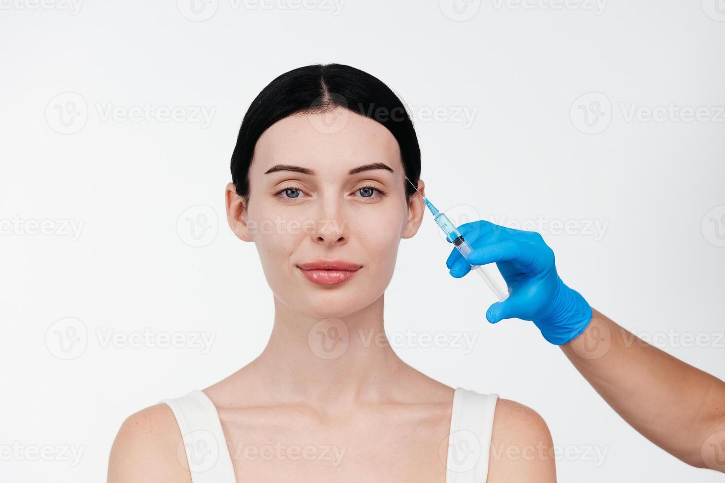 Unrecognizable lady receiving hyaluronic acid injection. Cropped picture of young woman standing isolated over white background. Doctor injecting in a beautiful face of a young woman. Plastic surgery photo