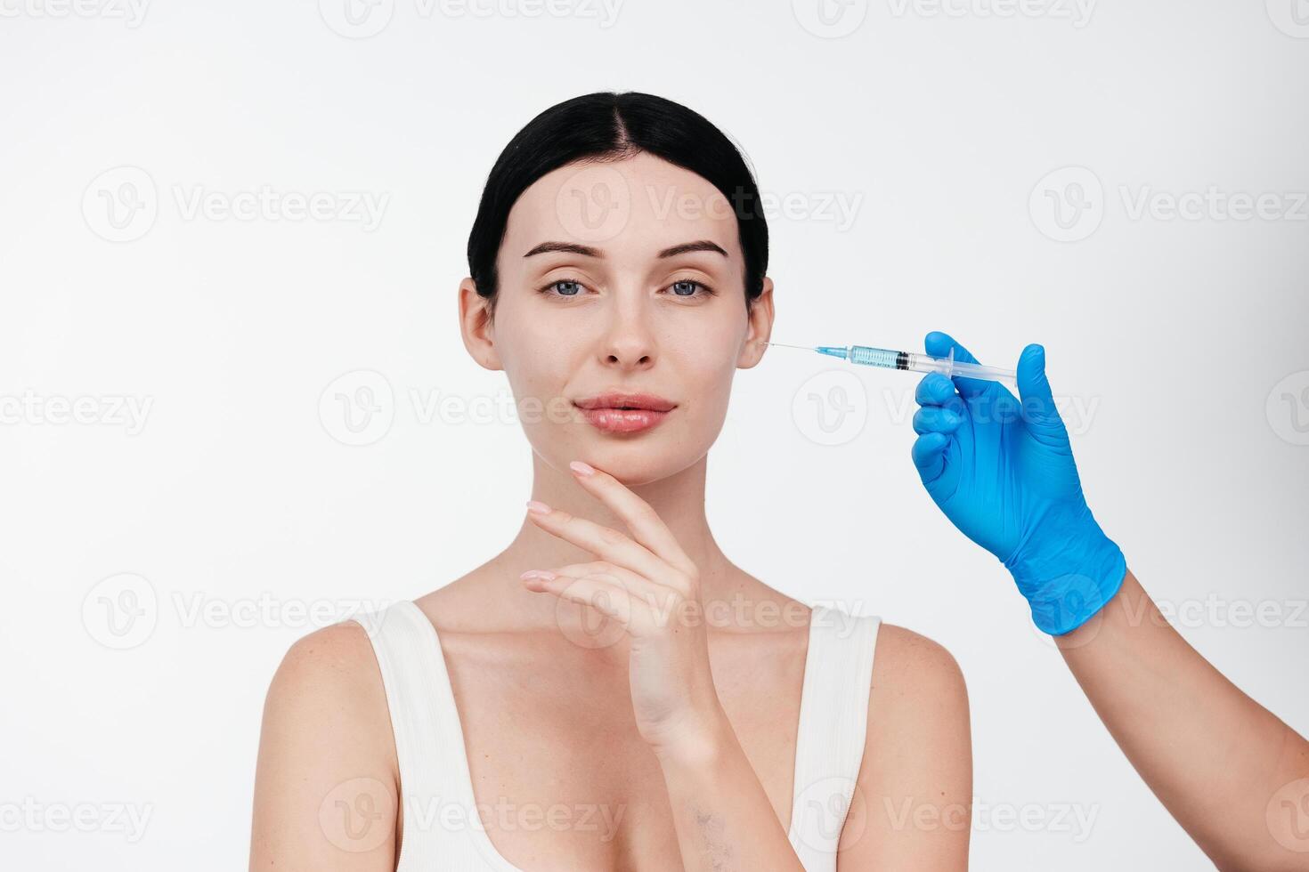 Unrecognizable lady receiving hyaluronic acid injection. Cropped picture of young woman standing isolated over white background. Doctor injecting in a beautiful face of a young woman. Plastic surgery photo