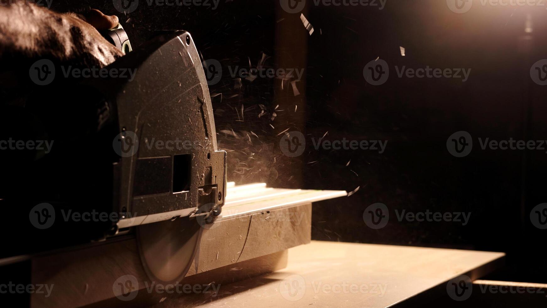 Close-up of a man cuts a wooden plank with an electric circular saw in a workshop. Cutting a piece of wood on a circular saw in backlight. Ideal topics related carpentry, efficient sawing techniques photo