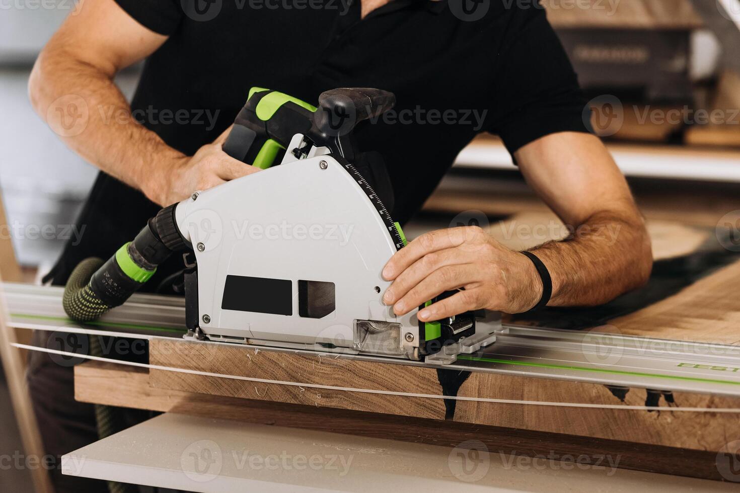 Unrecognizable man working with professional, electric circular saw, making a precise cut along the guide on a wooden surface. Tool is connected to a dust extraction system. Woodworking workshop. photo