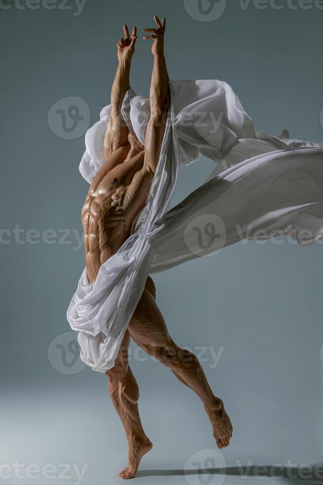 Athletic faceless man posing in a studio with a white cloth in an original way photo