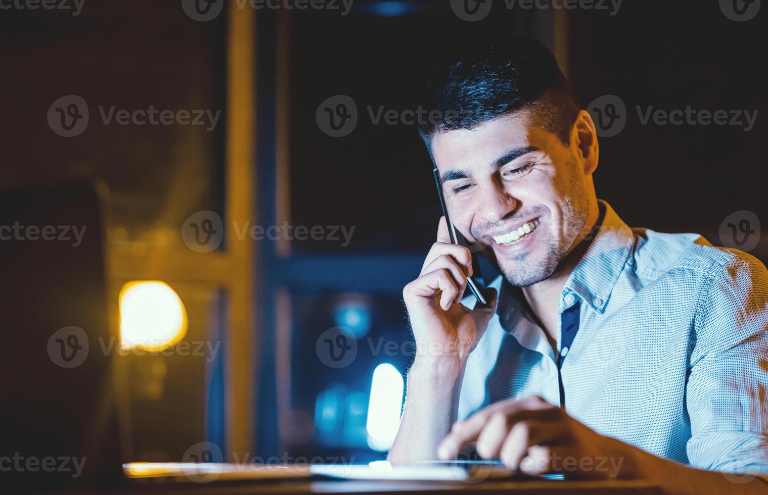 Happy Employee. Office Manager Talking On Cellphone Using Tablet Computer Working Overnight At Workplace. Copy Space photo