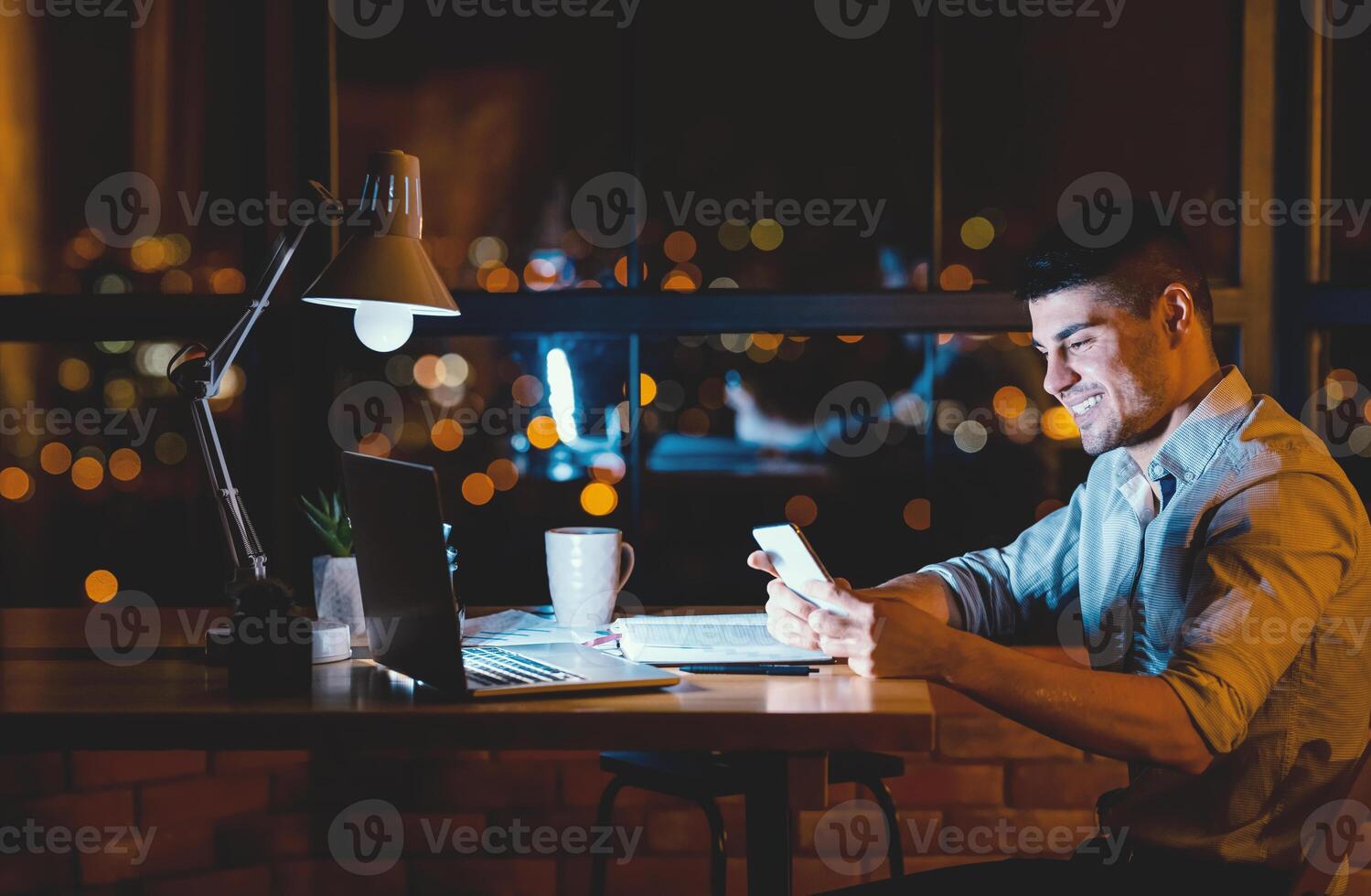Business Chat. Man Using Mobile Phone Texting Sitting At Laptop In Modern Office In The Evening. Copy Space photo