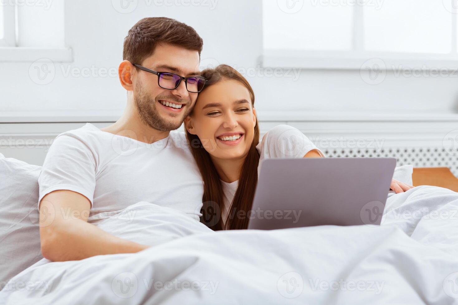 Weekend Together. Happy Couple Watching Film On Laptop Sitting In Bed At Home. Selective Focus photo