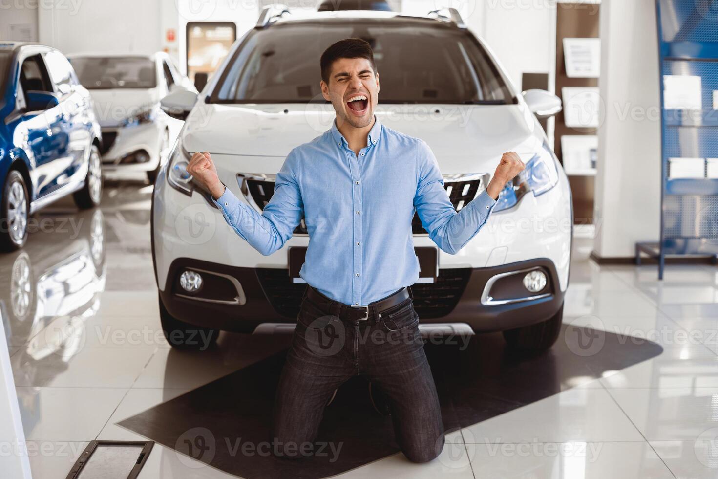 New Auto. Excited Man Shouting Shaking Fists Celebrating Buying New Car Standing On Knees In Dealership Store photo