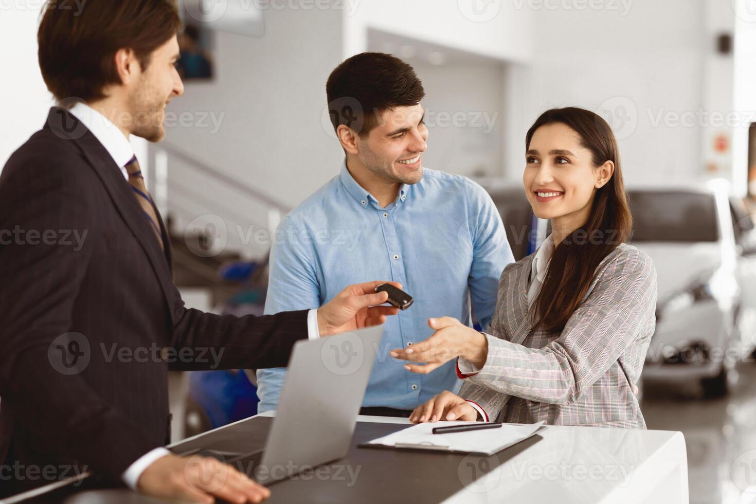 Car Sales. Manager Giving New Auto Key To Happy Couple Buying New Vehicle Standing In Dealership Shop photo
