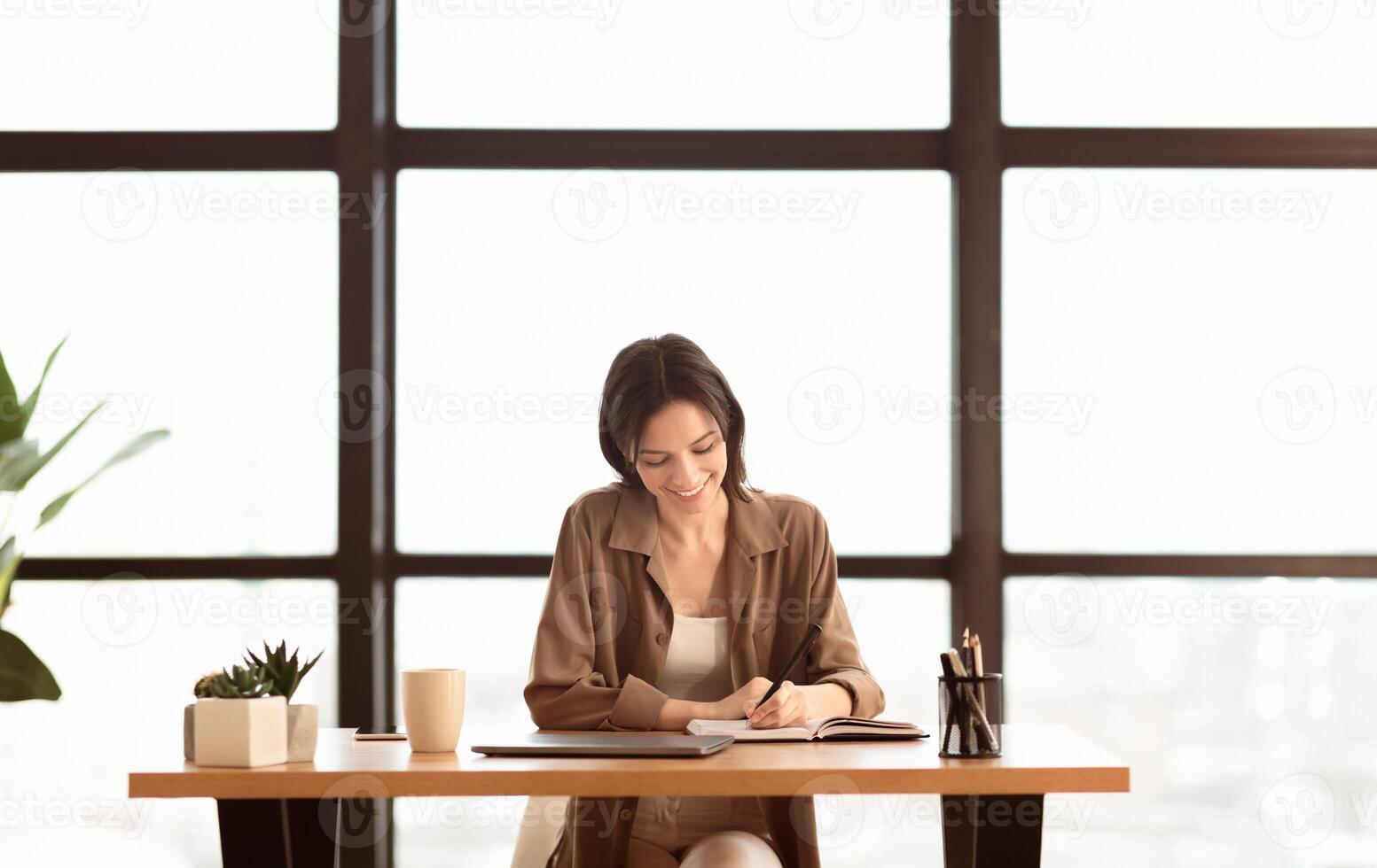 Happy Worker. Portrait of smiling female manager writing in notebook sitting at desk in modern office, copyspace photo