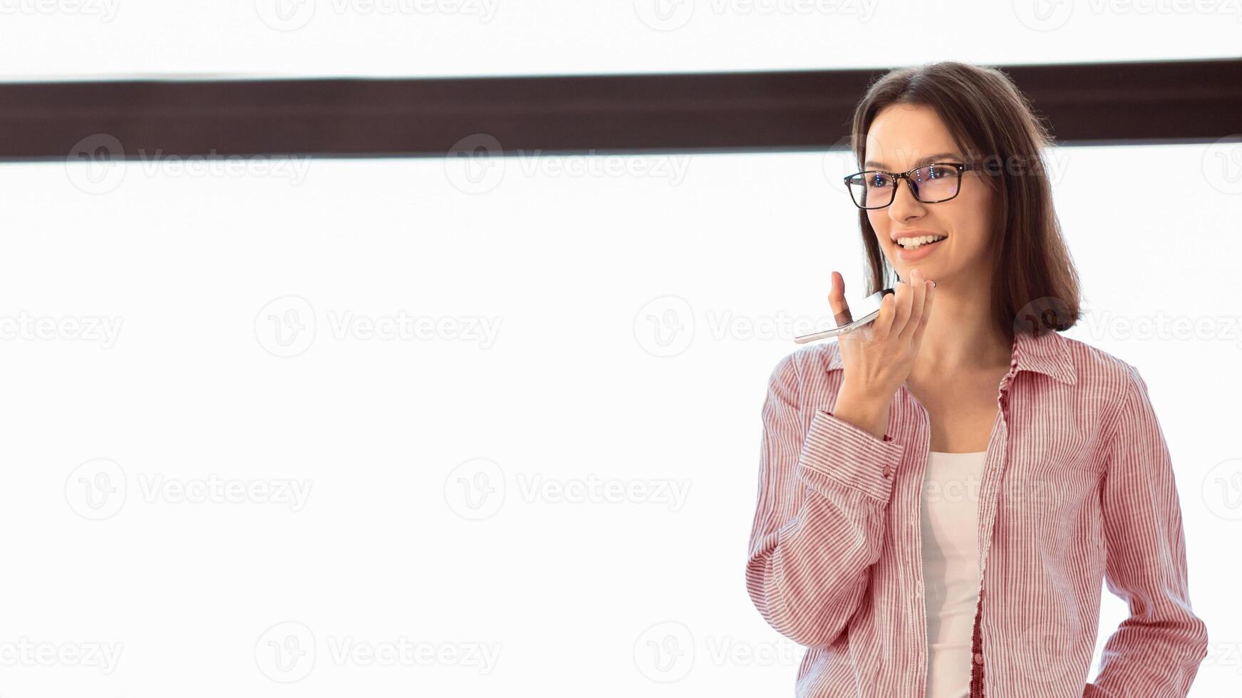 Technology And People Concept. Young female manager in specs using voice command recorder on mobile phone, copyspace photo