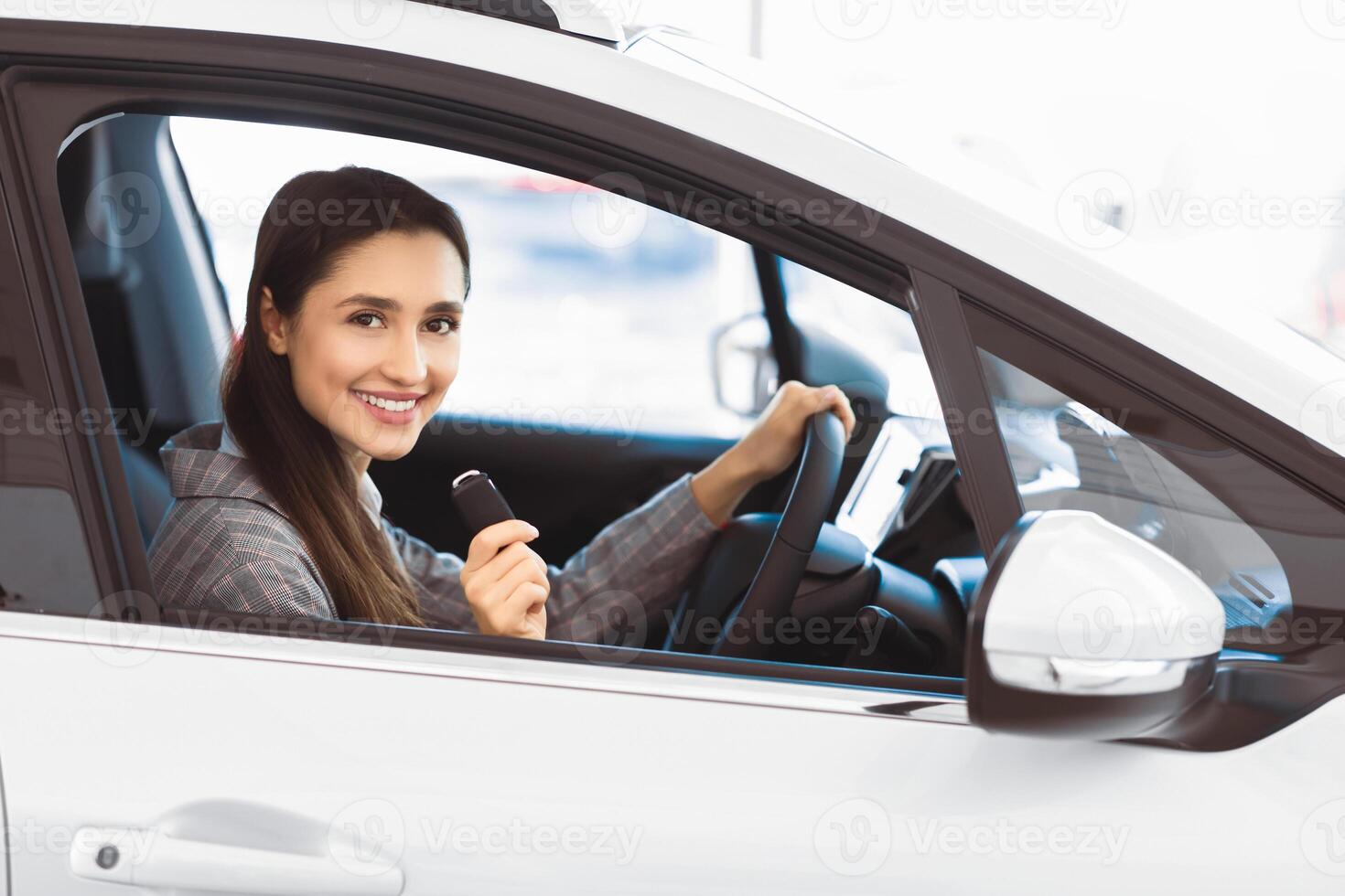 Joyful Woman Showing Car Key Smiling To Camera Sitting In Driver's Seat In New Automobile Dealership Store photo