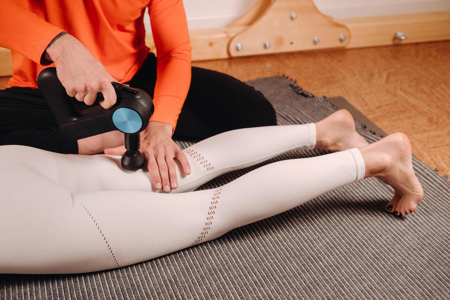 A male masseur massages a girl's body with a percussion massager to prepare for a stretching simulator photo