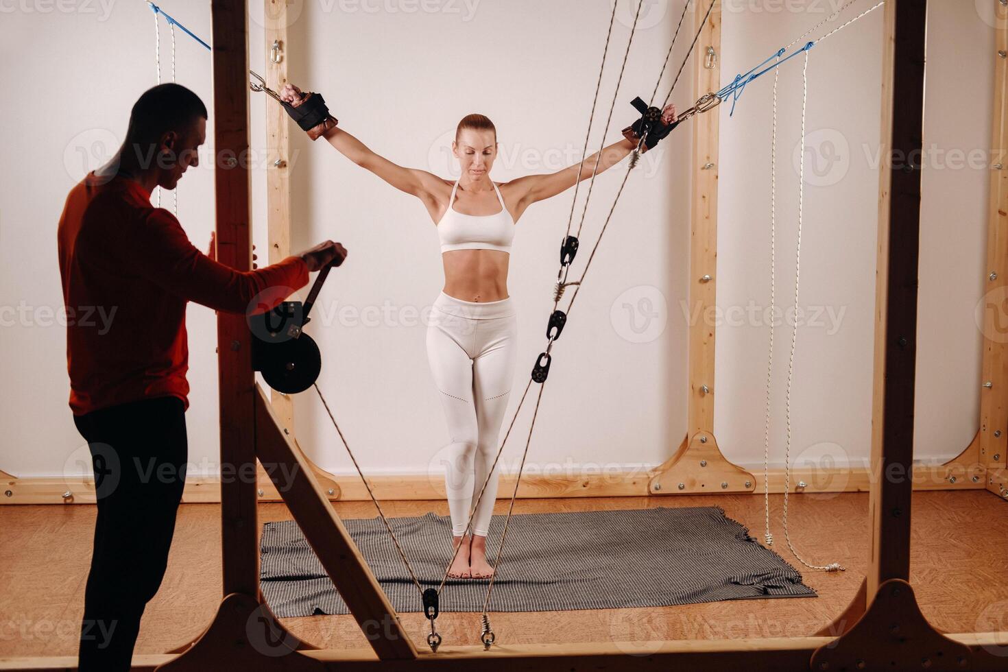 The trainer pulls the ropes stretching a Girl in a sports uniform on a simulator for stretching the human body photo