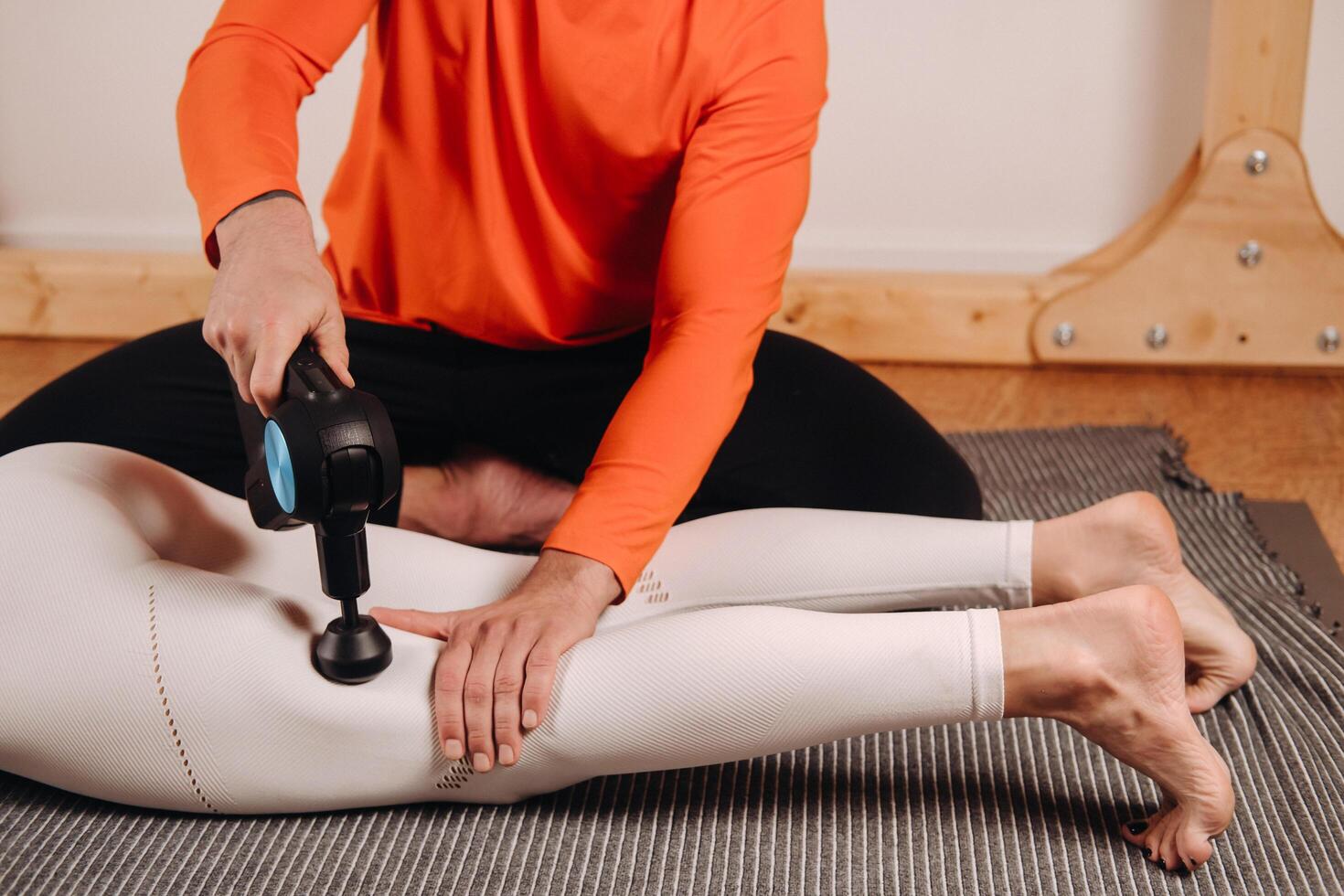 A male masseur massages a girl's body with a percussion massager to prepare for a stretching simulator photo