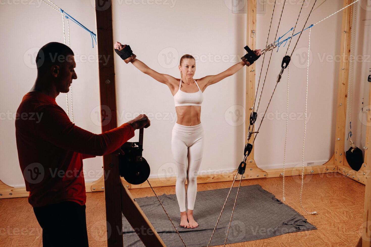 The trainer pulls the ropes stretching a Girl in a sports uniform on a simulator for stretching the human body photo
