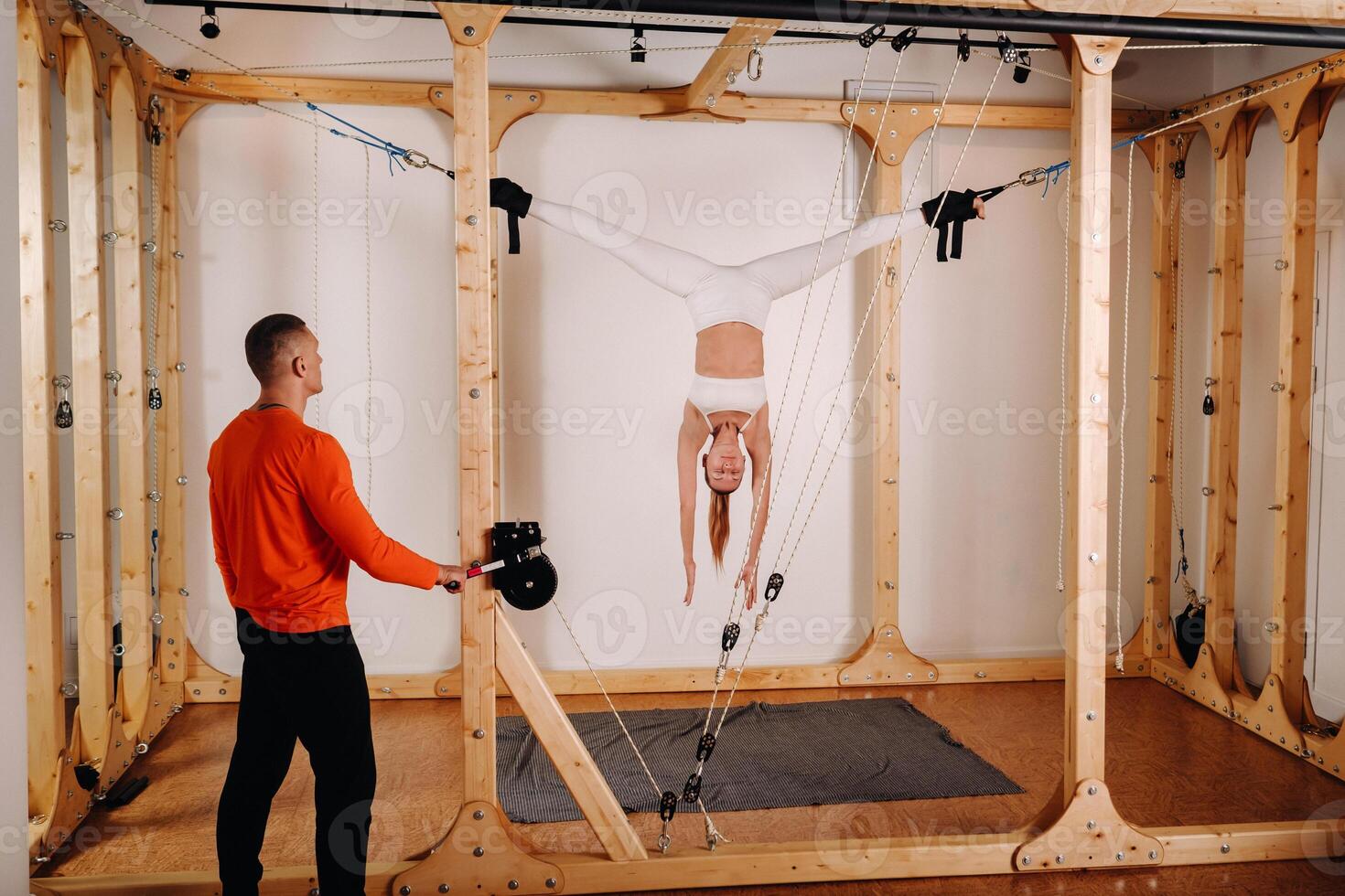 The trainer pulls the ropes stretching a Girl in a sports uniform on a simulator for stretching the human body photo