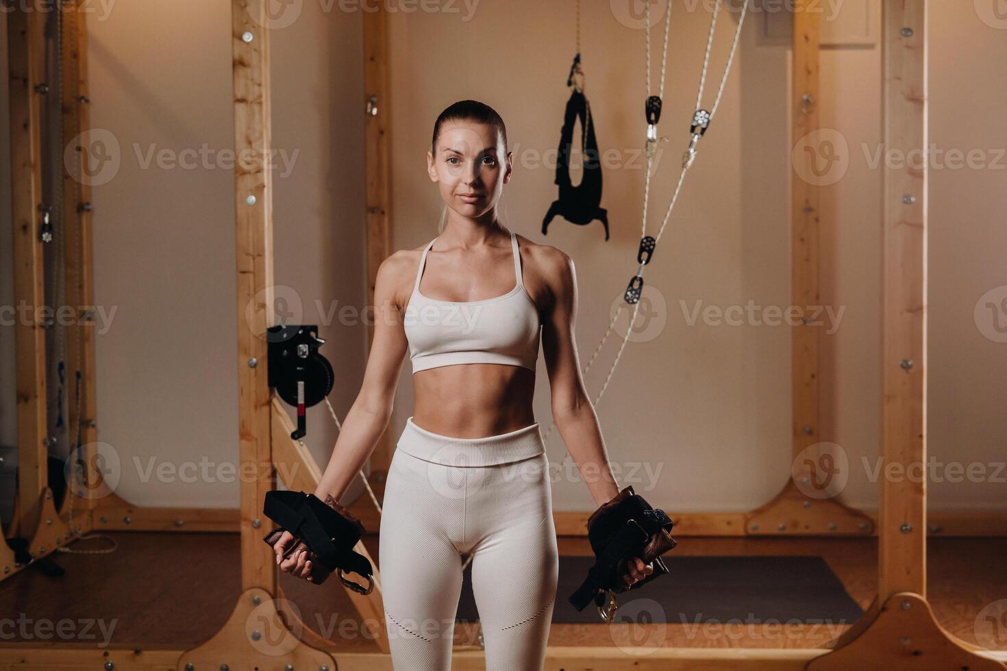 A girl in a sports uniform put devices on her hands for mounting on a simulator where she will do body stretching photo