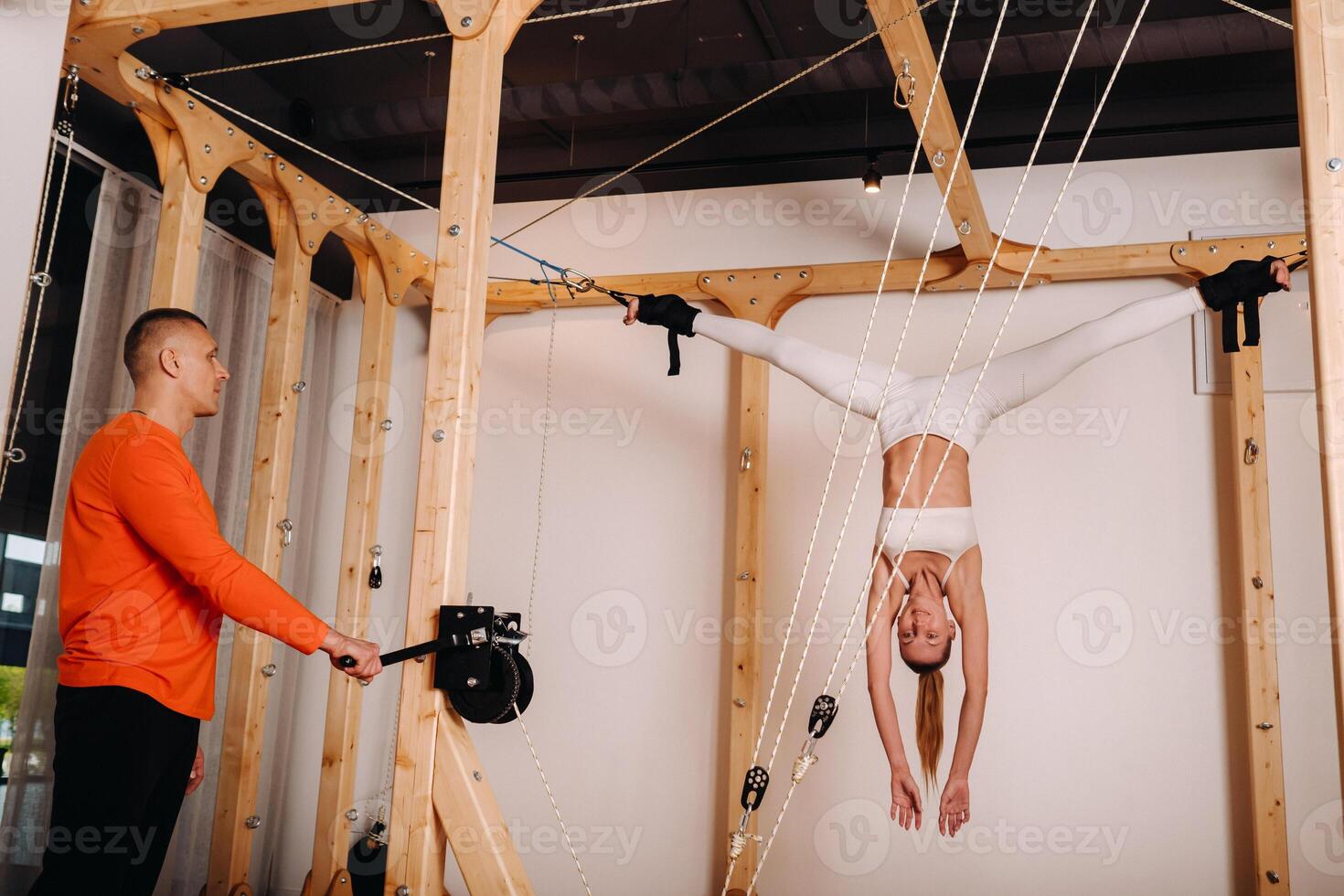 The trainer pulls the ropes stretching a Girl in a sports uniform on a simulator for stretching the human body photo