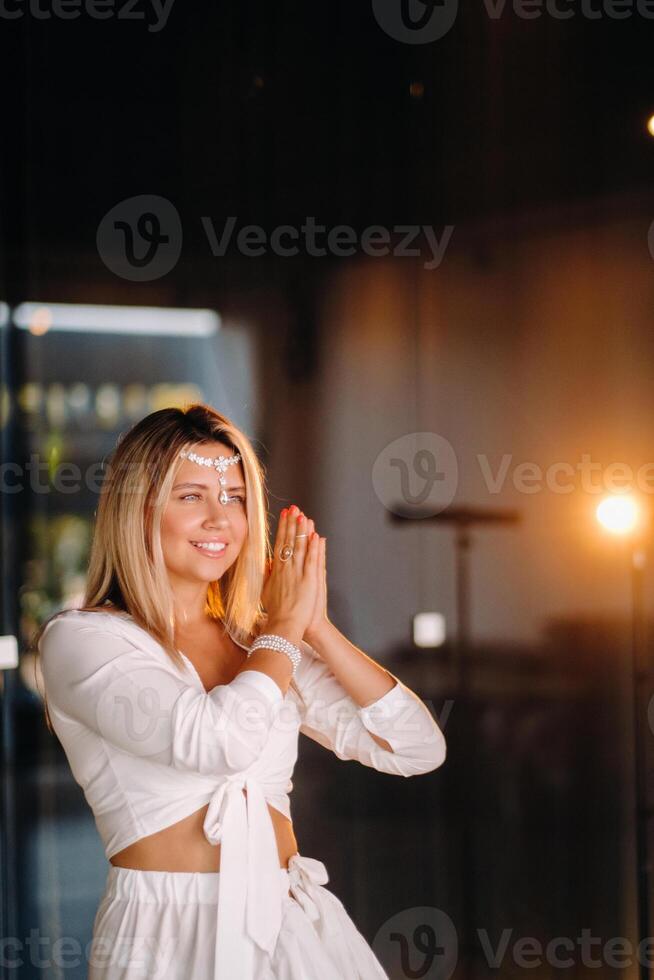 Portrait of a smiling girl in a white dress with her palms clasped in front of her photo