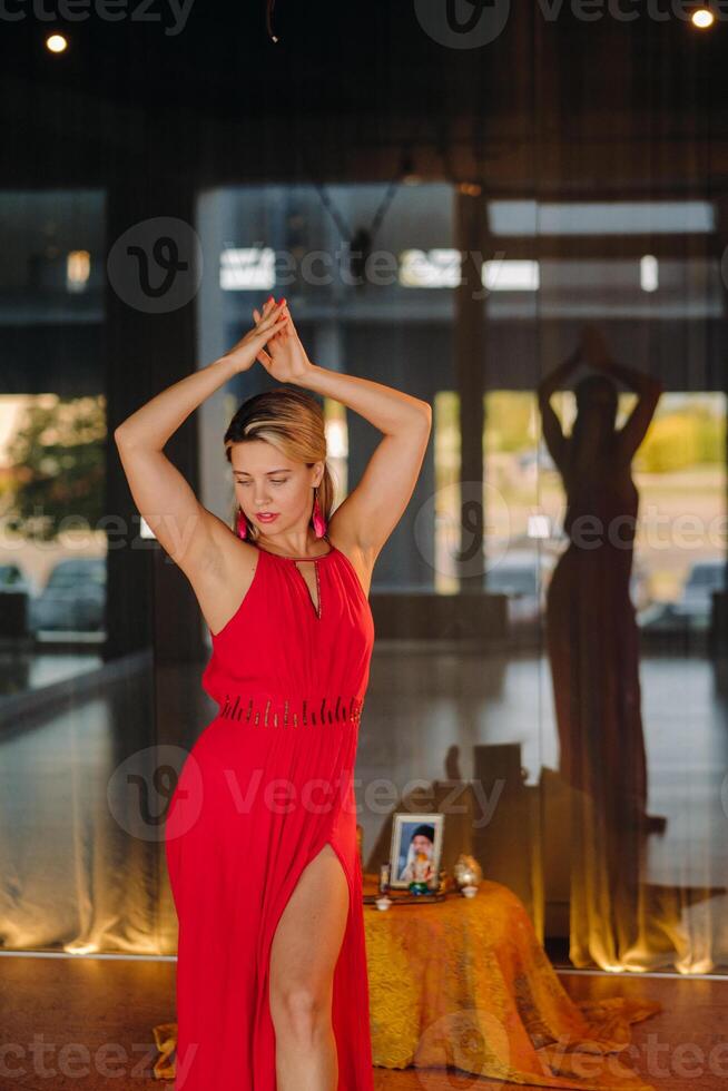 A girl in a red dress moves in a dance meditating indoors . Dynamic dance photo