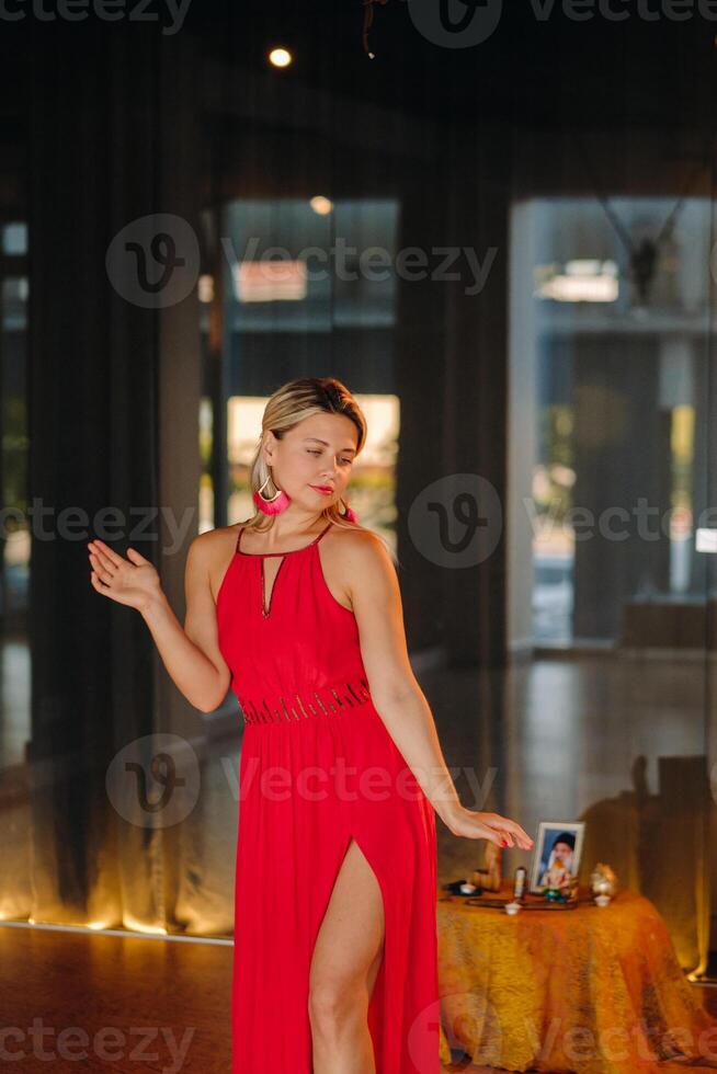 A girl in a red dress moves in a dance meditating indoors . Dynamic dance photo