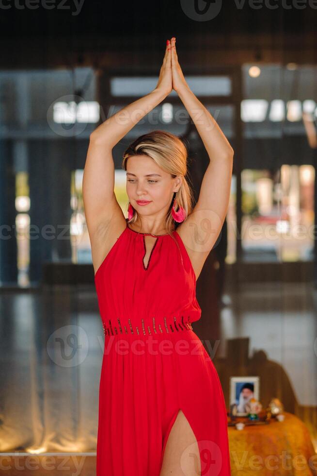 A girl in a red dress moves in a dance meditating indoors . Dynamic dance photo