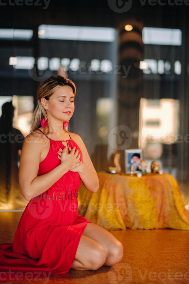 Meditation and concentration. a woman in a red dress, sitting on the floor with her eyes closed, is practicing medicine indoors. Peace and relaxation photo