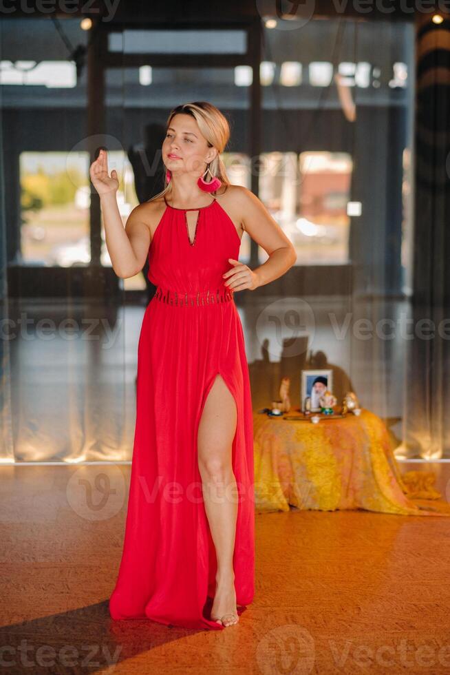 A girl in a red dress moves in a dance meditating indoors . Dynamic dance photo