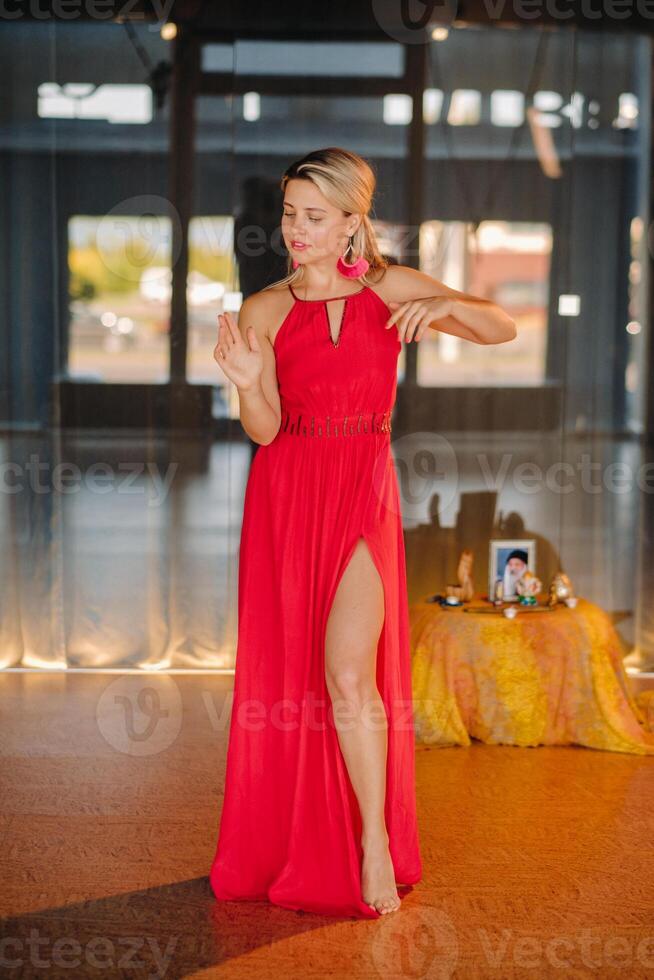A girl in a red dress moves in a dance meditating indoors . Dynamic dance photo