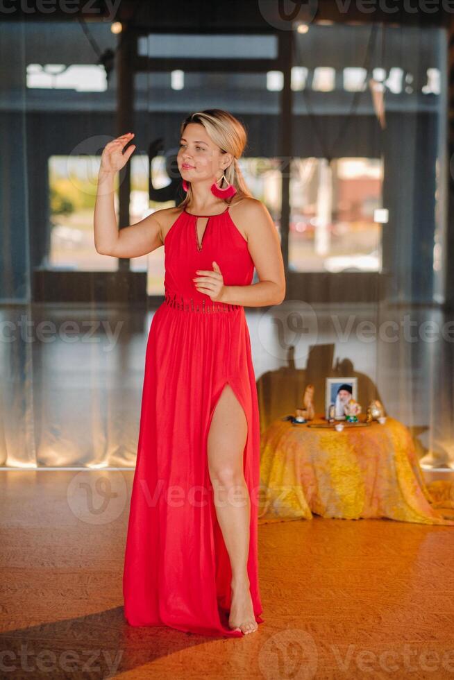 A girl in a red dress moves in a dance meditating indoors . Dynamic dance photo