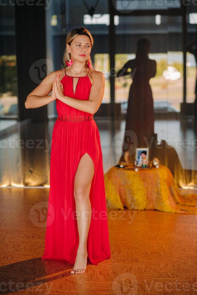 A girl in a red dress moves in a dance meditating indoors . Dynamic dance photo